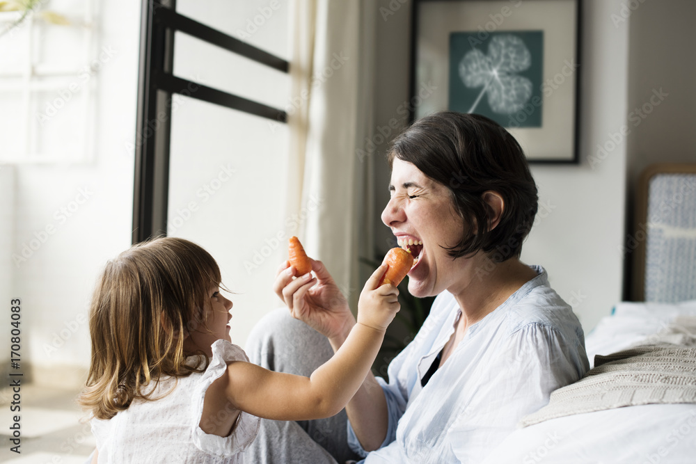 Mother and daughter eating carrot together Mother and daughter eating carrot together