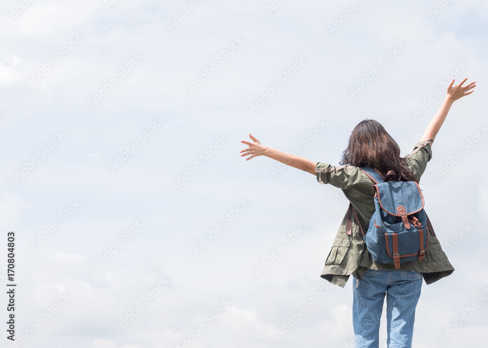 Back side of young girl with blue rucksack on her back wave hands up with blue sky Back side of young girl with blue rucksack on her back wave hands up with blue sky