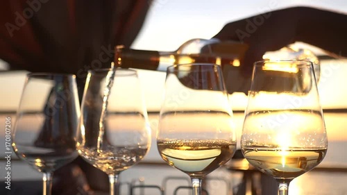 Pour tasty white wine in glass glasses with a reflection of the sunset and the sea in them. HD, 1920x1080. slow motion