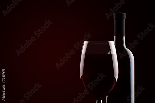 Bottle of red wine and a glass of red wine on a dark background.
