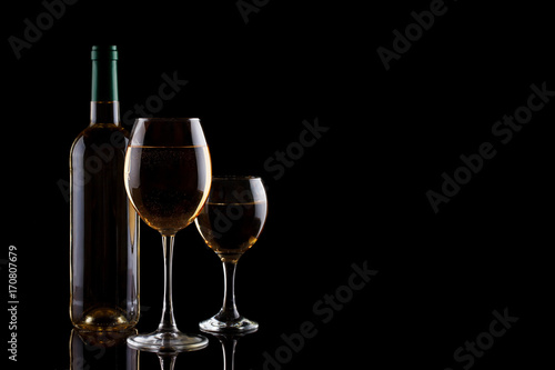 A bottle of white wine and two glasses with white wine on a dark background.