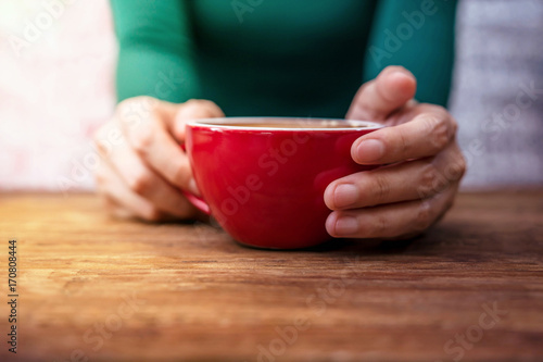 Woman Relax in Cafe or House, Coffee Cup in hand on Wooden Table, Front view, Contrasting Color Tone, Selective focus on cup