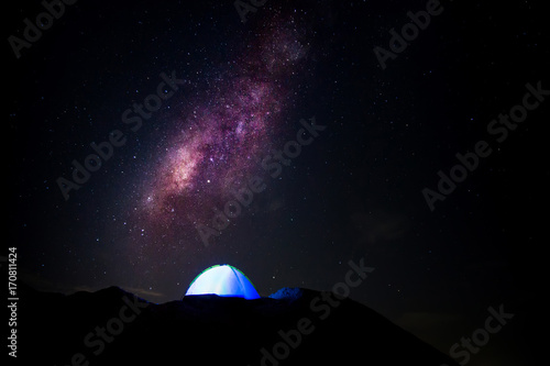 Milky way and blue tent with light on the hill.