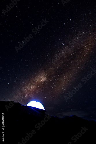 Milky way and blue tent with light on the hill.