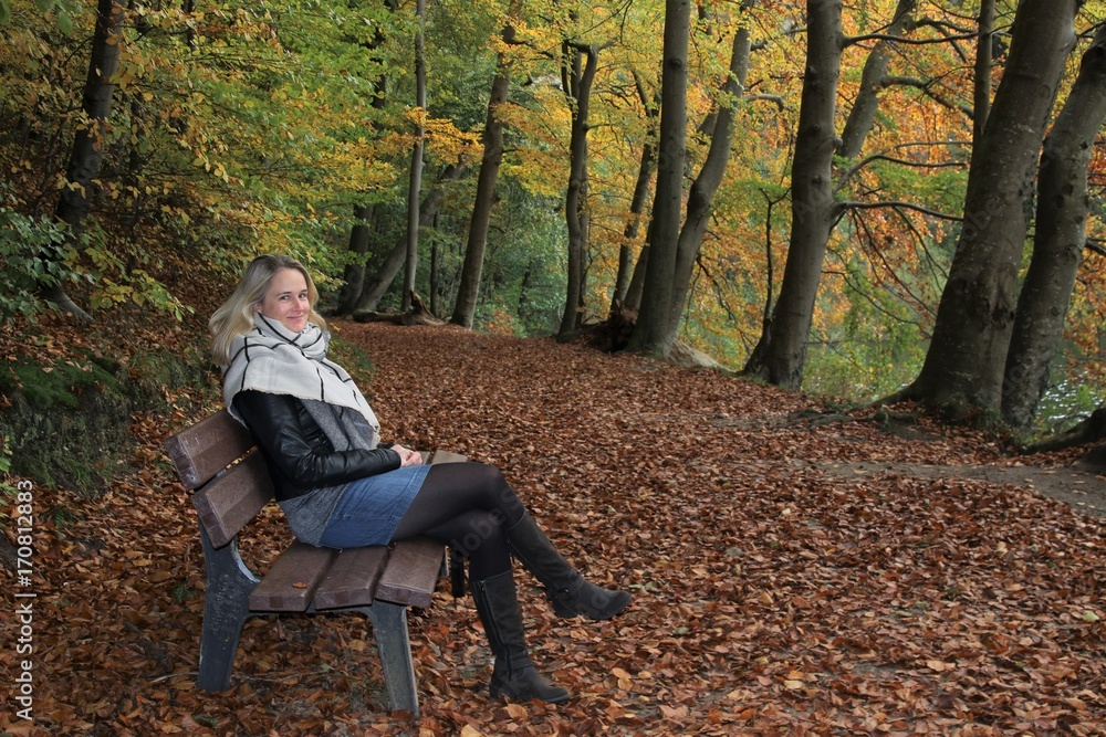 attraktive blonde Frau sitzt im Herbst auf einer Bank im Wald attraktive blonde Frau sitzt im Herbst auf einer Bank im Wald