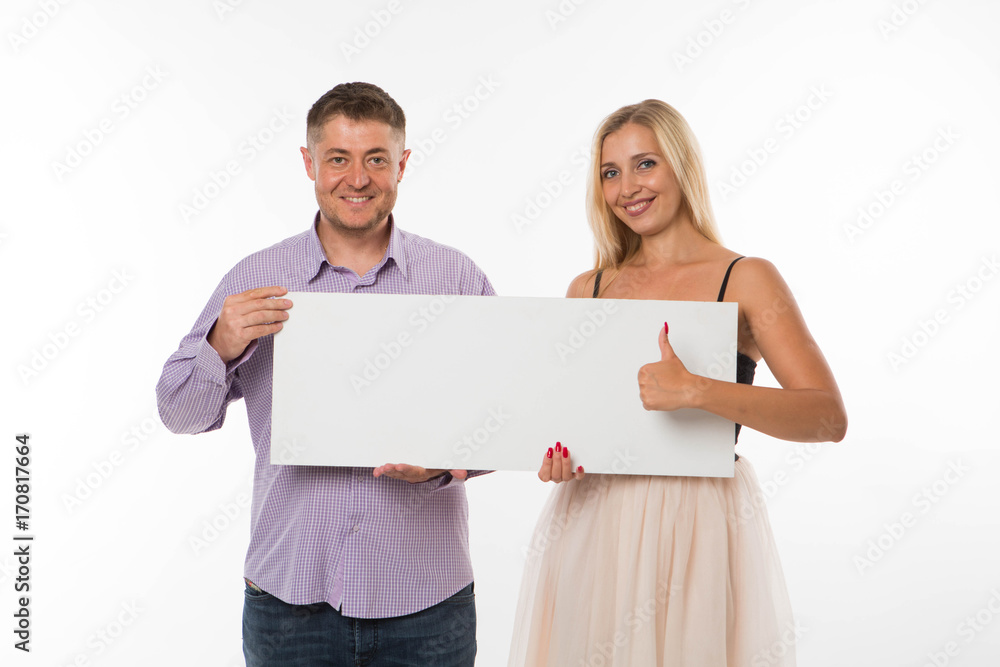 Young happy couple portrait of a confident businessman showing presentation, pointing placard gray background. Ideal for banners, registration forms, presentation, landings, presenting concept. Young happy couple portrait of a confident businessman showing presentation, pointing placard gray background. Ideal for banners, registration forms, presentation, landings, presenting concept.