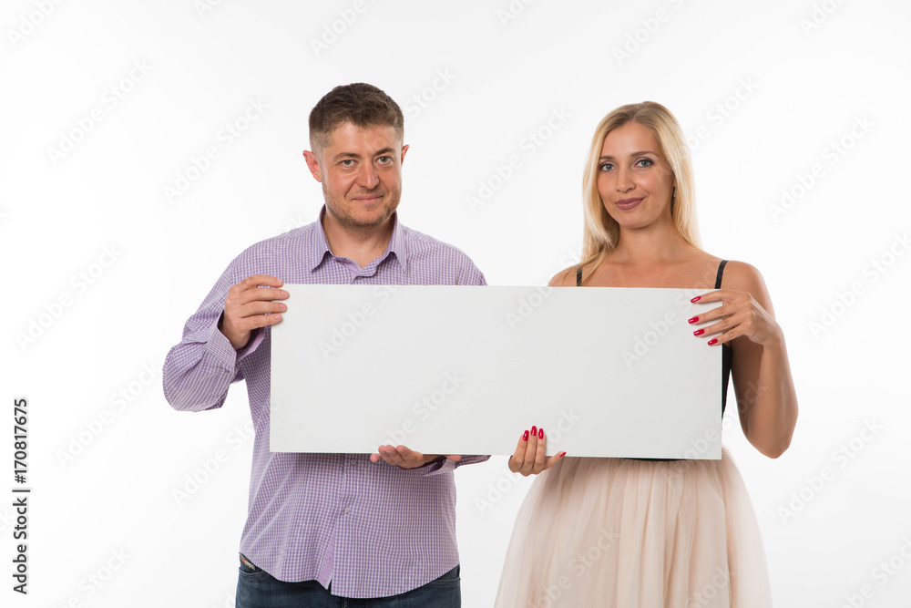 Young glad couple portrait of a confident businessman showing presentation, pointing paper placard gray background. Ideal for banners, registration forms, presentation, landings, presenting concept. Young glad couple portrait of a confident businessman showing presentation, pointing paper placard gray background. Ideal for banners, registration forms, presentation, landings, presenting concept.
