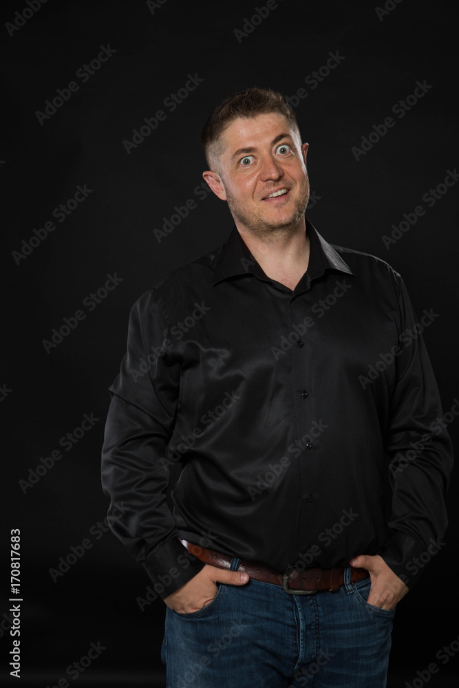 Young surprised man portrait of a confident businessman showing by hands on a black background. Ideal for banners, registration forms, presentation, landings, presenting concept.