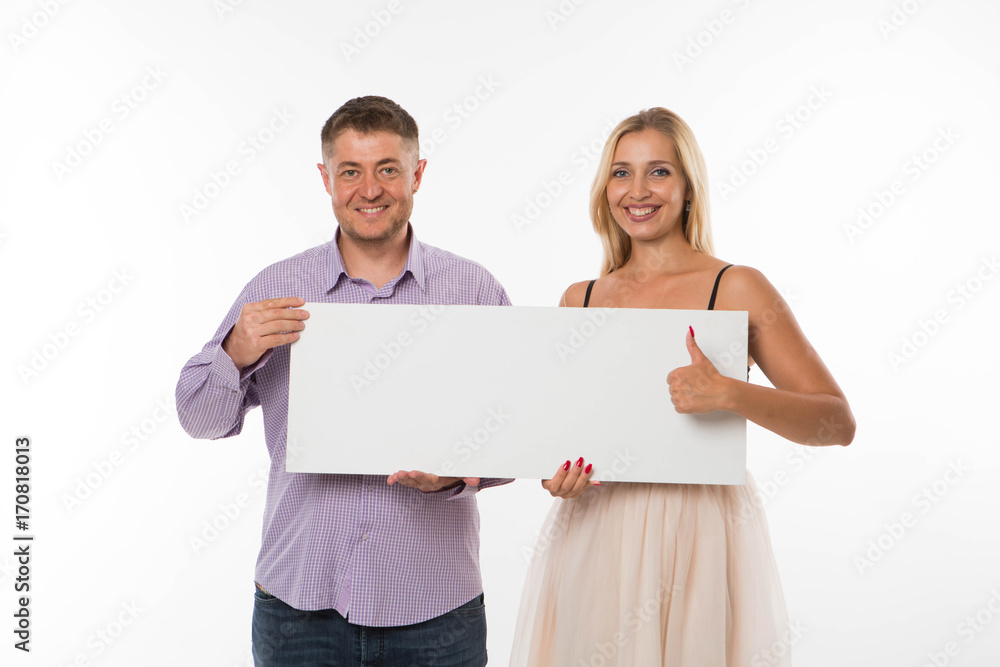 Young happy couple portrait of a confident businessman showing presentation, pointing placard gray background. Ideal for banners, registration forms, presentation, landings, presenting concept. Young happy couple portrait of a confident businessman showing presentation, pointing placard gray background. Ideal for banners, registration forms, presentation, landings, presenting concept.