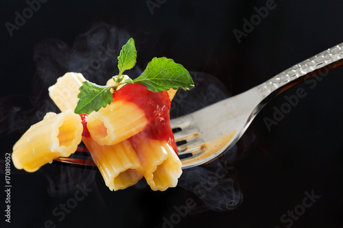 Fork with  rigatoni and basil on black background