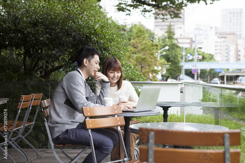 A young couple talking while watching a laptop on the cafe terrace