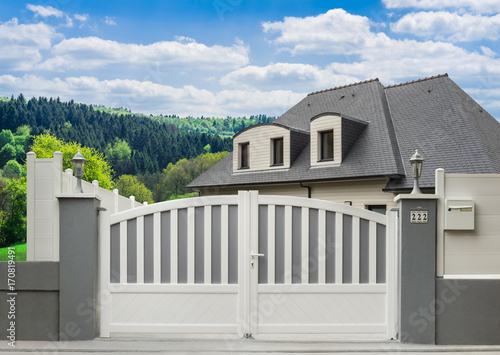 Fotótapéta Modernes PVC-Gartentor in grau und weiß und Einfamilienhaus in schöner Landschaf