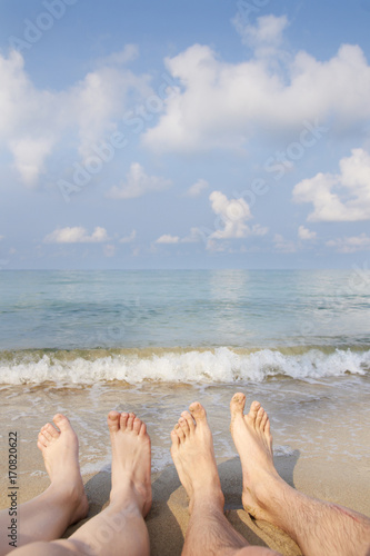 Two people legs on sea beach. Blue sky with clouds