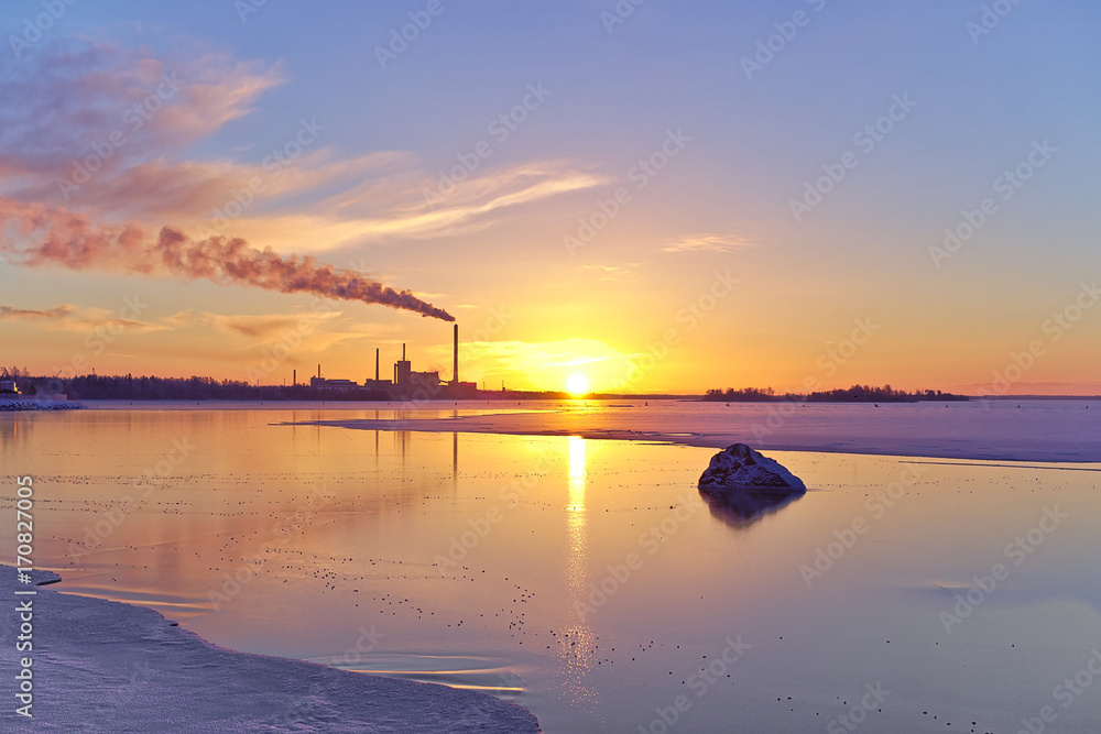 Beuatiful seaside winter sunset with a smoking factory chimney. Urban nature background.