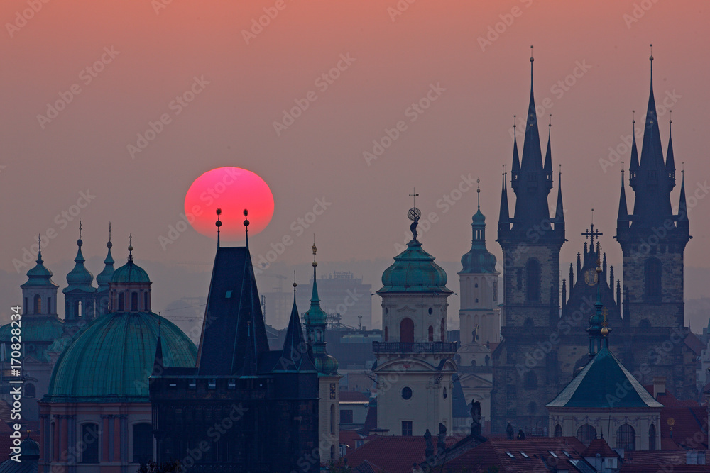 Twilight in historical city. Magical picture of tower with orange sun in Prague, Czech Republic, Europe. Beautiful detailed sunrise view of Prague church towers. Early morning colours with old town.