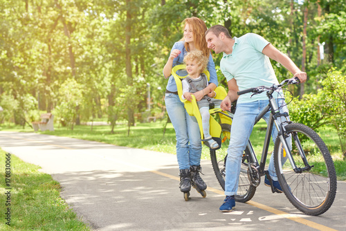 Happy active family enjoying rollerblading and cycling at the park in the summer copyspace sport recreation activity enjoyment children safety seat marriage love emotions.