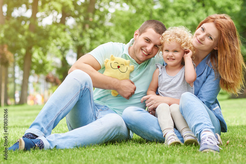 Shot of a happy young family sitting on the grass at the park together smiling to the camera copyspace lifestyle leisure weekend holidays love parenting parents children kids emotions.  © serhiibobyk