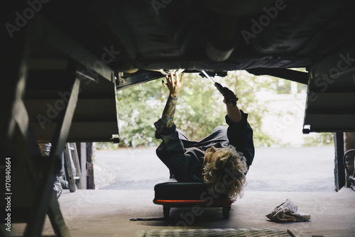 Underneath view of female mechanic repairing car at repair shop
