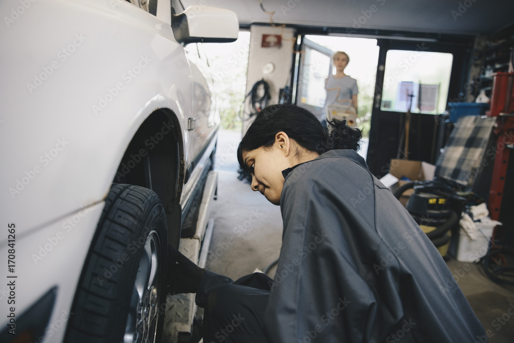 Female mechanic examining car wheel at auto repair shop Female mechanic examining car wheel at auto repair shop