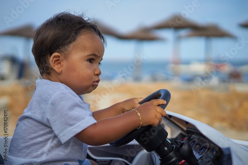 Young boy driving toy car along beachfront.