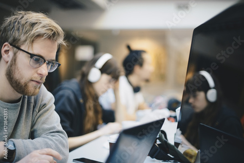 Male programmer working on computer with colleagues at desk in office photo