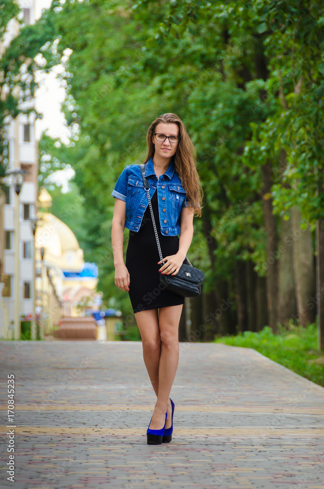 Beautiful woman in a short black dress and glasses walks in the summer in the park