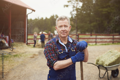 Portrait of confident farmer holding pitchfork while standing in farm photo