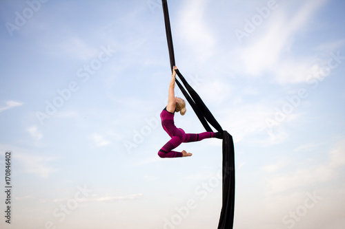 exercises with aerial silk outdoor, sky background. beautiful fit woman training acrobatic in airt. 