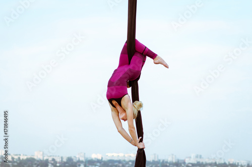 exercises with aerial silk outdoor, sky background. beautiful fit woman training acrobatic in airt.  photo