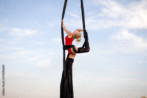 exercises with aerial silk outdoor, sky background. beautiful fit woman training acrobatic in airt.  photo