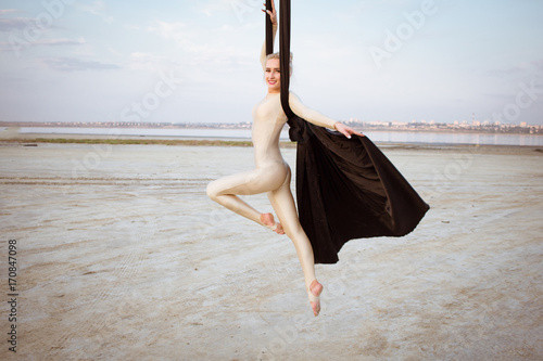 exercises with aerial silk outdoor, sky background. beautiful fit woman training acrobatic in airt.  photo