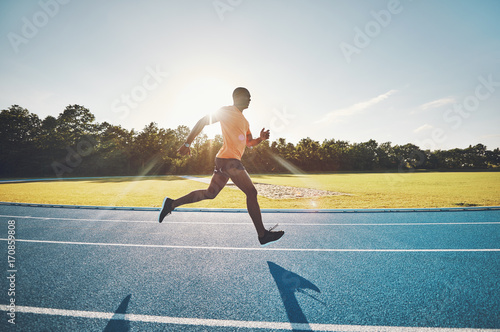 Fotografi Lone athlete sprinting along a track on a sunny day