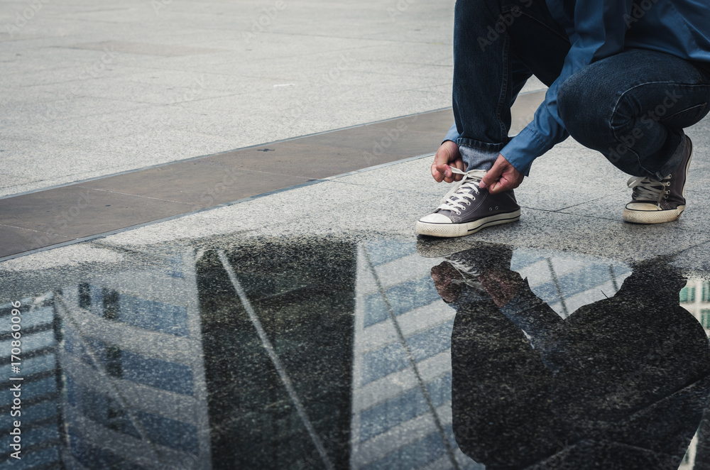 handsome man sit on concrete floor tying shoelace to wearing the shoes with water reflection on floor. handsome man sit on concrete floor tying shoelace to wearing the shoes with water reflection on floor.
