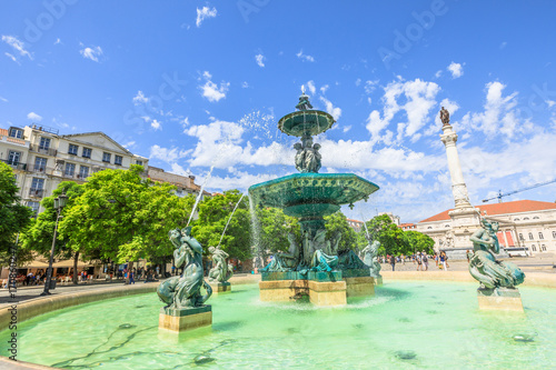 One of two baroque fountains in Praca Dom Pedro IV or Rossio Square in Lisbon downtown  Portugal  Europe. The National Theater D. Maria II and statue of Dom Pedro IV on background. Sunny day.