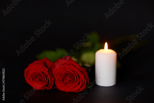red roses and burning candle over black background