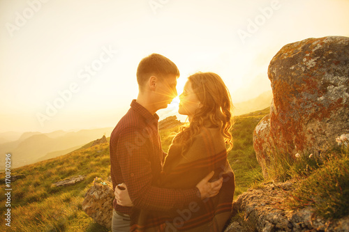 Young happy couple kissing in nature against the setting sun at sunset.