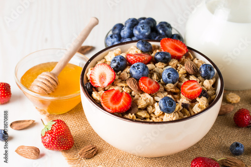 Healthy breakfast concept with oat flakes and fresh berries on rustic background. Food made of granola, muesli. Healthy banana smoothie with blackberries, muslie, strawberries, blueberries and honey. photo