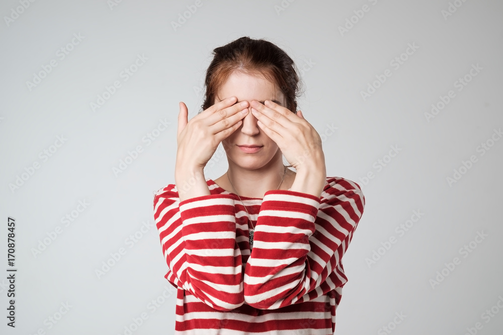 Young woman covering face with hands on gray background. Young woman covering face with hands on gray background.
