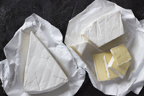 Camembert or brie cheese in white paper on black  background. Top view.