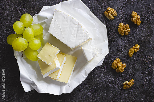 Camembert or brie cheese in white paper, walnut and green grape on black  background.