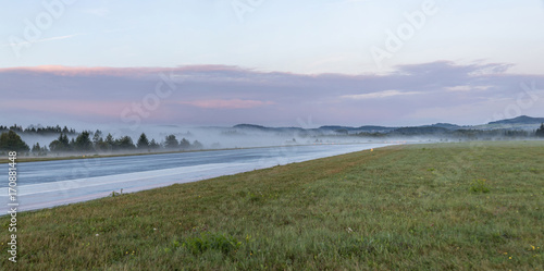 Empty runway at airport during a foggy sunrise
