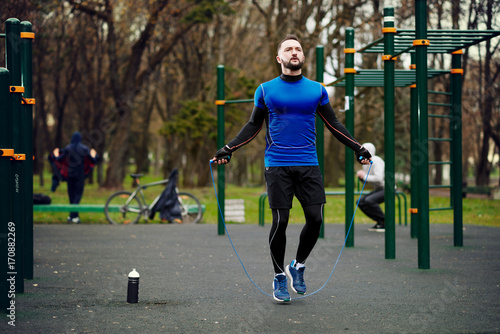 Young strong man jumping with rope on sports field in the street in the summer