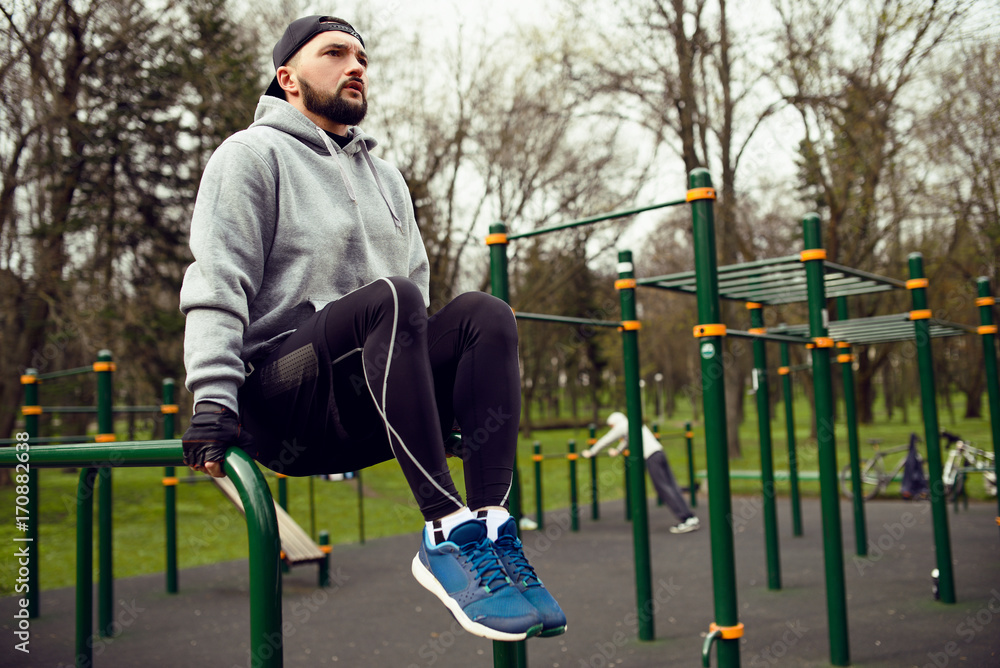 Young strong man doing abs exercises on the uneven bars on the sports field in the summer in the city Young strong man doing abs exercises on the uneven bars on the sports field in the summer in the city