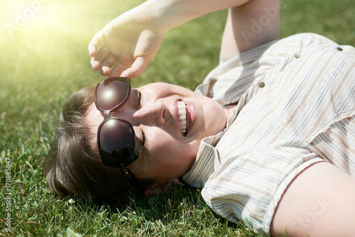 Woman squint from the bright sun, lie on green grass, city park, summer outdoor