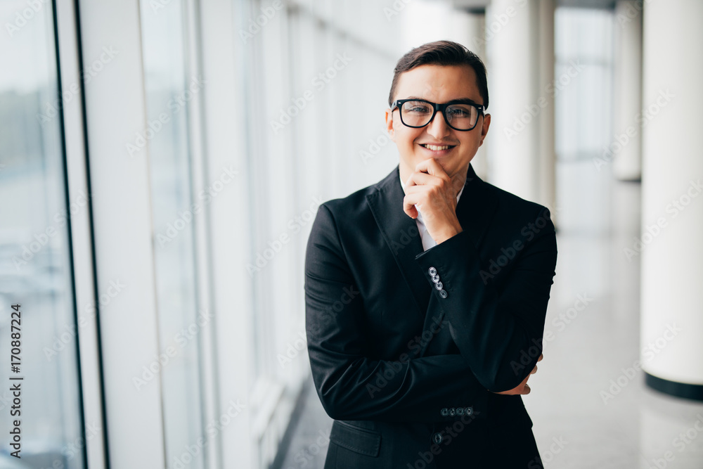 Portrait of Smiling businessman standing near the window in office with hands on chin Portrait of Smiling businessman standing near the window in office with hands on chin
