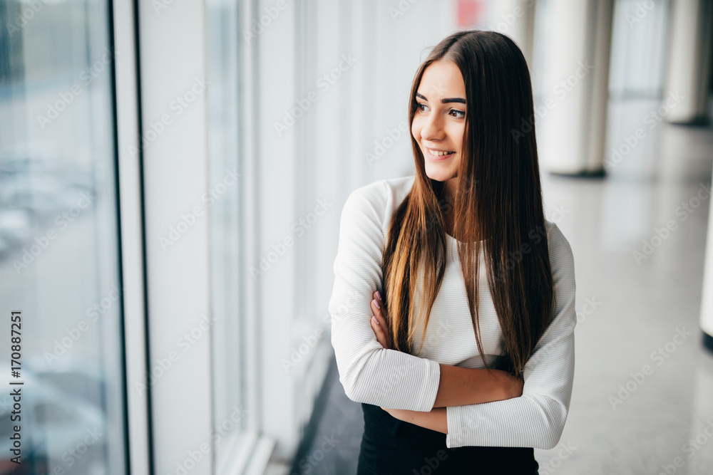 Portrait of attractive businesswoman standing in front of windows in an office building overlooking the city Portrait of attractive businesswoman standing in front of windows in an office building overlooking the city