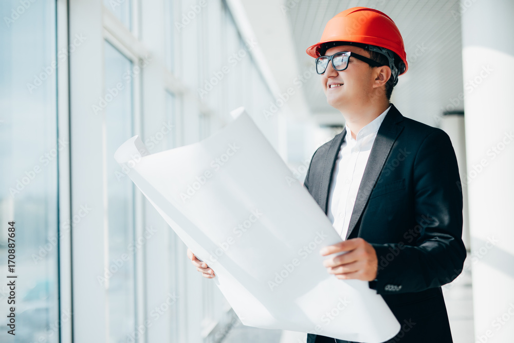 Builder engineer man wear security helmet look at blueprint paper construction near panoramic windows Builder engineer man wear security helmet look at blueprint paper construction near panoramic windows