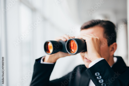 Business man looking with binoculars over panoramic windows photo