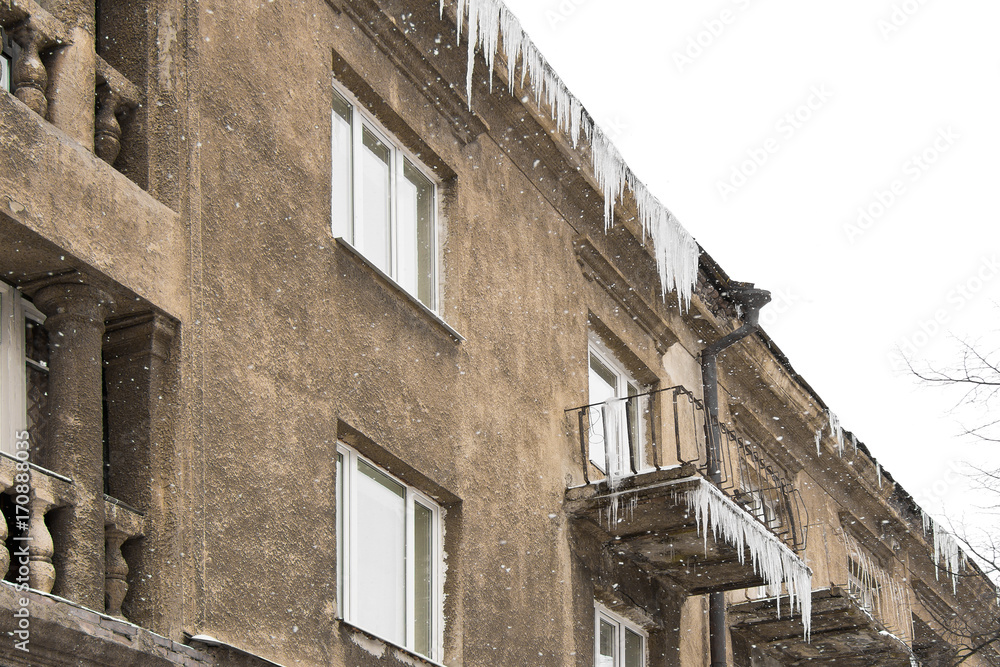 Dangerous long icicles hanging on the roof and balcony of the old building in winter