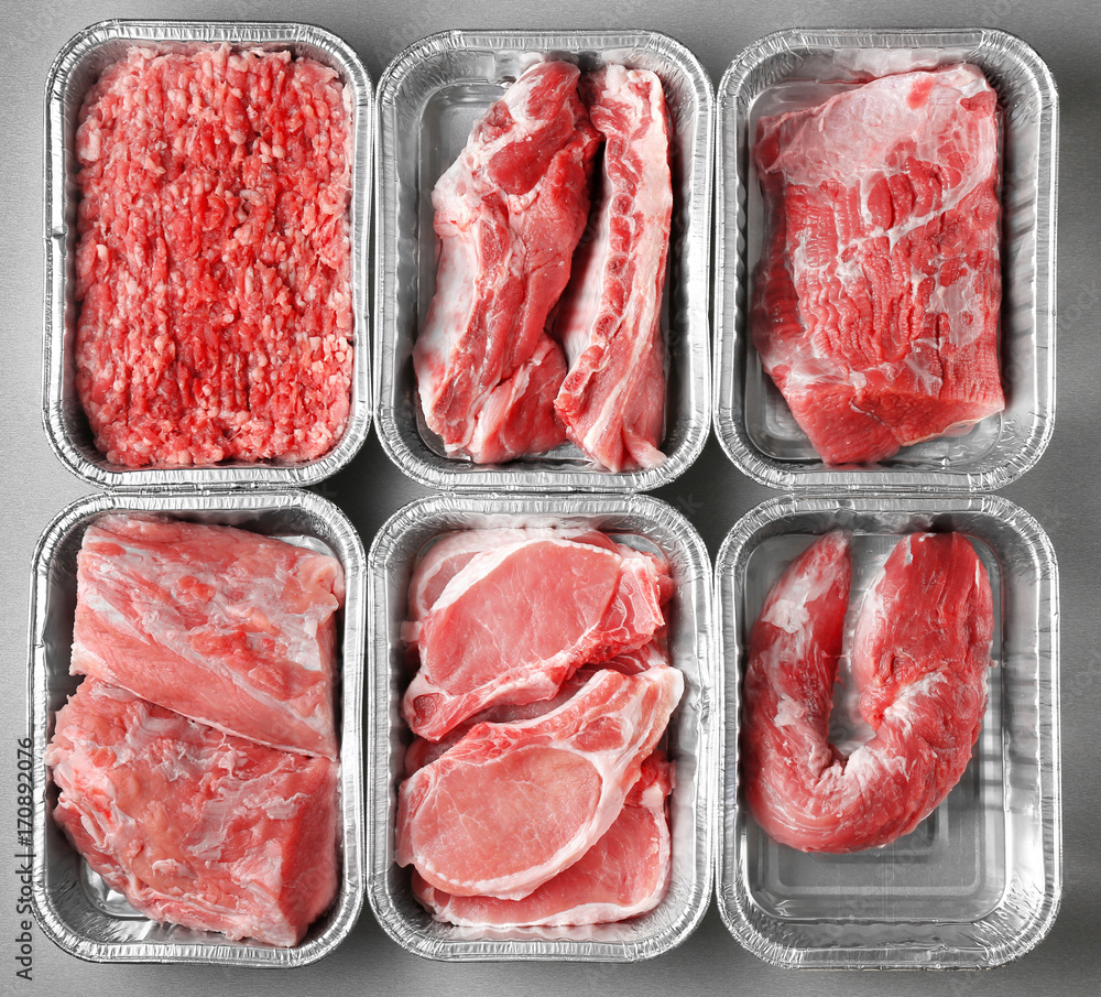 Containers with pieces of different fresh meat on grey background Containers with pieces of different fresh meat on grey background